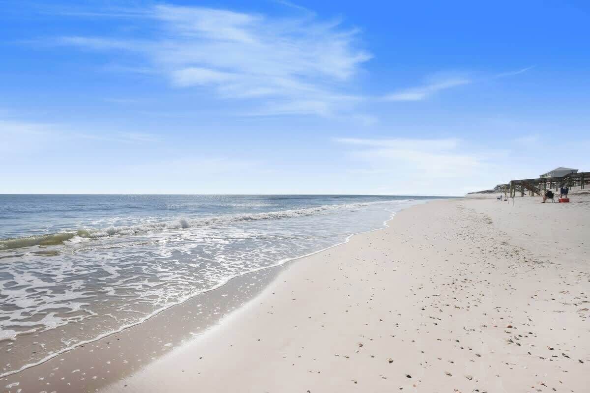 A beach with a clear sky, calm sea, and a structure with a roof on the right.
