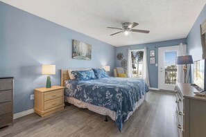 A bedroom with a bed, nightstands, a dresser, a ceiling fan, and a door leading to a balcony.