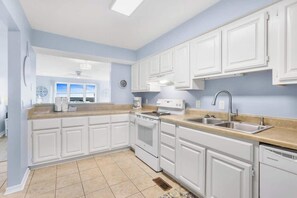 A kitchen with white cabinets, a stove, a sink, and a window.