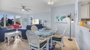 Un salon moderne avec une table à manger au plateau en verre, des chaises en osier blanc, un fauteuil rouge et un ventilateur de plafond.