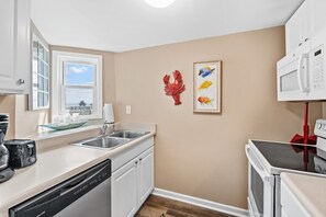 A kitchen with a dishwasher, a microwave, and a stove. There is a window with a view of the beach.