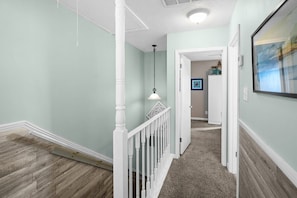 A hallway with a wooden floor, white railing, and a hanging light fixture.