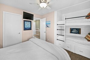 Ein Schlafzimmer mit einem Einzelbett, einem Etagenbett, einem Deckenventilator und einer Tür zu einem anderen Raum.