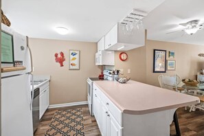 Una cocina compacta con armarios blancos, una isla central y una zona de comedor con mesa y sillas.