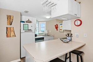 Una cocina con armarios blancos, encimera blanca, un lavabo y un reloj en la pared.