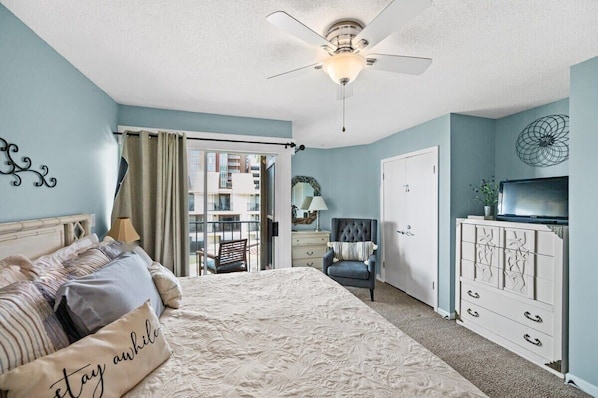 A bedroom with a bed, a ceiling fan, a dresser, a chair, and a TV.