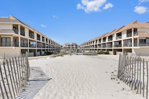 A beachfront hotel with multiple balconies, a sandy beach in front, and a clear blue sky.