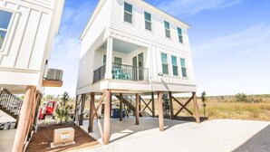 Een twee verdiepingen tellend strandhuis met balkon, houten terras en overdekte entree.