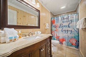 A bathroom with a wooden vanity, a sink, a mirror, and a shower curtain with a beach theme.