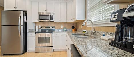 Una cocina moderna con armarios blancos, electrodomésticos de acero inoxidable, encimeras de granito y piso de madera.