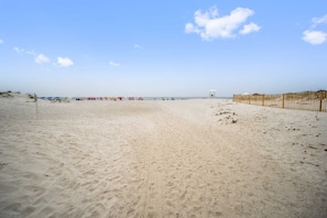 A beach with a sandy shore, a wooden fence, and beach umbrellas in the distance.