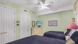 Une chambre à coucher comprenant un lit, une commode, un ventilateur de plafond et des éléments de décoration murale.