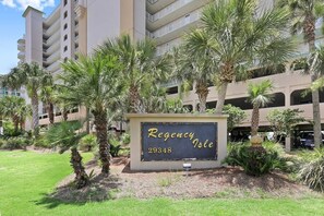Naamplaatje voor 'Regency Isle' met het nummer 29348, omringd door palmbomen en een gebouw met meerdere balkons op de achtergrond.