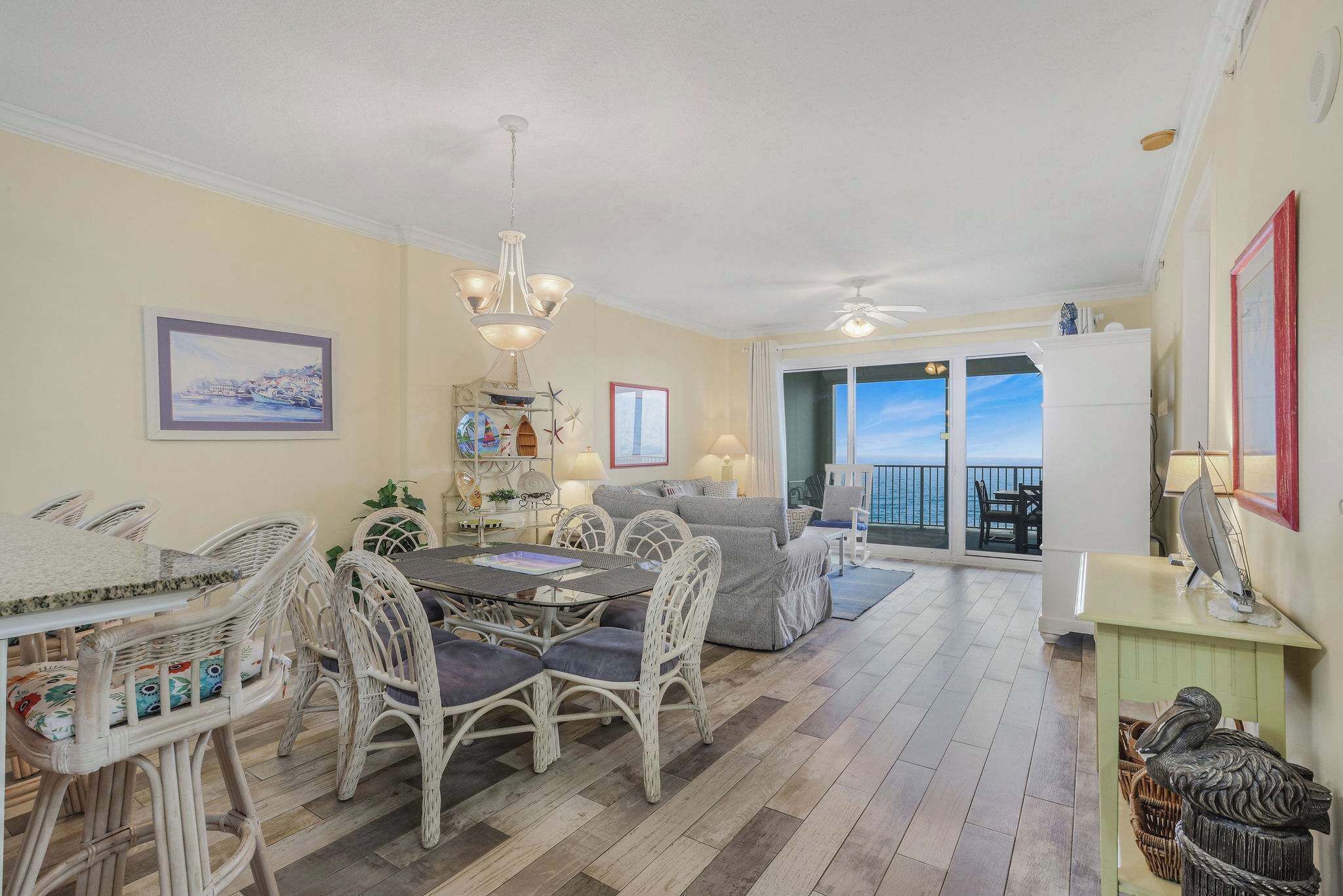 A dining area with wicker chairs and a table, a sofa, and a view of the sea through a balcony.