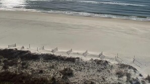 Ein Strand mit blauem Himmel, ruhiger See und einem Sandufer mit Strandsonnenschirmen.
