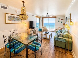 Ein Wohnzimmer mit einem Glastisch, einer Couch, einem Fernseher und einem Balkon mit Meerblick.