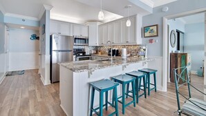 Cocina con armarios blancos, encimera de granito y taburetes de bar color turquesa.