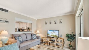 A living room with a sofa, coffee table, TV, and decorative items. - Gulf Tower 12A: Beachfront Bliss for 6! (Gulf Shores)