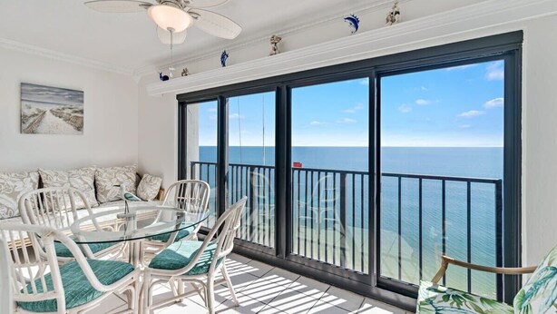 A balcony with a view of the ocean, furnished with white chairs and a glass table, and a ceiling fan above. - Gulf Tower 12A: Beachfront Bliss for 6! (Gulf Shores)