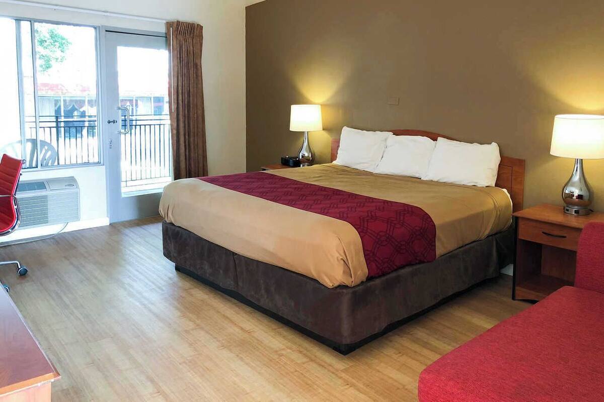Habitación de hotel con una cama grande, dos lámparas de noche, un escritorio de madera, una silla y un balcón con vistas.