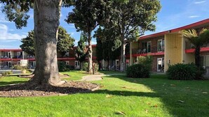 Un edificio de techo rojo y múltiples ventanas. Un árbol está en primer plano y un camino conduce al edificio.