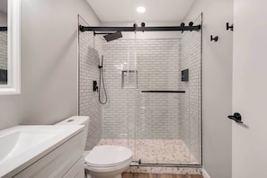 Un baño moderno con una bañera blanca, un inodoro y una zona de ducha con mampara de vidrio y pared azulejada.