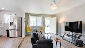 Ein modernes Wohnzimmer mit einer Couch, einem Couchtisch, einem Fernseher und einer integrierten Küchenzeile mit Kühlschrank.