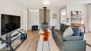 Ein modernes Wohnzimmer mit Kamin aus Stein, einem Glastisch und einem grauen Sofa.
