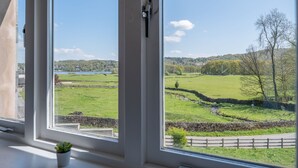 A view from a window overlooking a green landscape with a stone wall and a body of water in the distance. - Cunsey Lodge with Woodfired Hot Tub and stunning views (Cunsey)