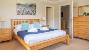 A neatly made bed with a blue blanket, wooden headboard, and checkered pillows. There is a wooden nightstand with a lamp and a wooden dresser with drawers. - Cunsey Lodge with Woodfired Hot Tub and stunning views (Cunsey)