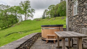 Un bâtiment en pierre avec une table et des bancs en bois, un jacuzzi et un mur en pierre.