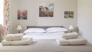 Une chambre d’hôtel avec un lit, deux lampes de chevet, une fenêtre avec des rideaux et trois œuvres d’art encadrées accrochées au mur.