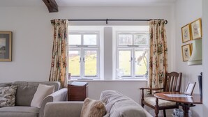 Un salon chaleureux avec un canapé, une chaise en bois, une petite table et une fenêtre ornée de rideaux à motifs floraux.