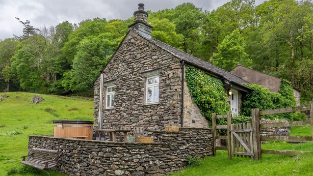 Une maison en pierre avec un toit en pente, un porche en bois et un mur de pierre.