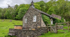 Une maison en pierre avec un toit en pente, un porche en bois et un mur de pierre.