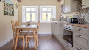 Une cuisine avec une table et des chaises, une fenêtre avec des rideaux et un mur recouvert de carreaux.