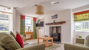 A cozy living room with a fireplace, a television, and a dining area with a table and chairs. - Eel House Cottage - sleeps 4 guests  in 2 bedrooms (Graythwaite)