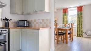 A kitchen with a microwave, stove, and cabinets. There is a dining area with a table and chairs. - Eel House Cottage - sleeps 4 guests  in 2 bedrooms (Graythwaite)