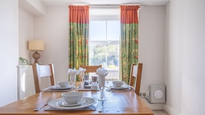 A dining room with a wooden table set for four, a window with curtains, and a lamp on a side table. - Eel House Cottage - sleeps 4 guests  in 2 bedrooms (Graythwaite)