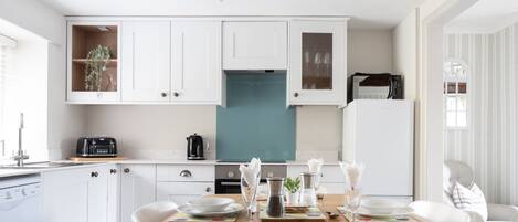 A modern kitchen with white cabinets, a teal backsplash, and a dining area set for four with white plates and cutlery.