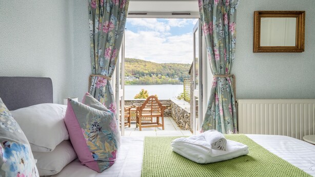 Een slaapkamer met een bed, kussens, een groene mat en uitzicht op een meer en heuvels.