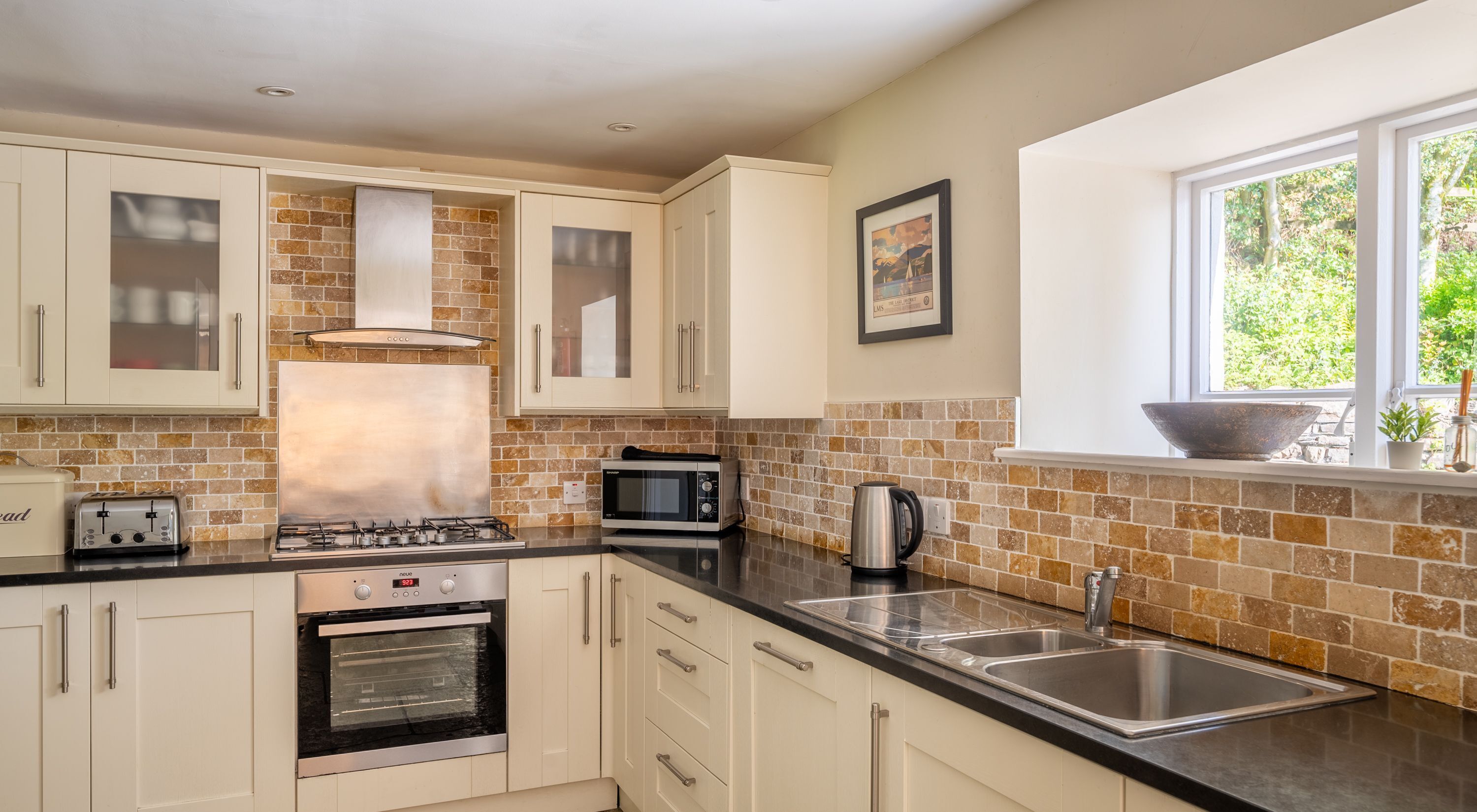 A modern kitchen with white cabinets, a gas stove, a built-in oven, a microwave, and a double sink.