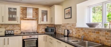 A modern kitchen with white cabinets, a gas stove, a built-in oven, a microwave, and a double sink.