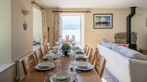 A dining room with a long wooden table set for a meal, a stone fireplace, and a view of the outdoors. - Stunning Lake fronted Property with Hot Tub - Hammerhole (Cunsey, Graythwaite)