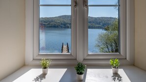 A window with a view of a lake, a dock, and a forested hill. - Stunning Lake fronted Property with Hot Tub - Hammerhole (Cunsey, Graythwaite)