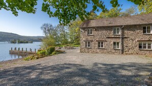 A stone building with multiple windows, a gravel driveway, and a wooden dock extending into a lake. - Stunning Lake fronted Property with Hot Tub - Hammerhole (Cunsey, Graythwaite)