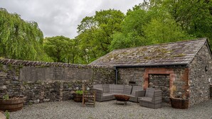 A stone building with a sloped roof, surrounded by gravel and greenery.