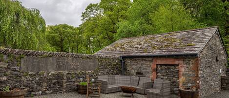 A stone building with a sloped roof, surrounded by gravel and greenery.