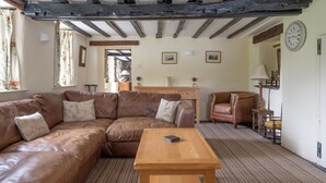 A cozy living room with a brown leather sofa, a wooden coffee table, and a traditional wooden chair. - Lakeshore cottage with Hot Tub - Hullet Hall (Graythwaite)