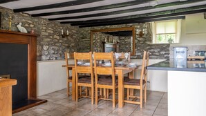 A rustic kitchen with a stone wall, wooden dining table, and chairs. A bread dispenser is visible on the counter. - Lakeshore cottage with Hot Tub - Hullet Hall (Graythwaite)